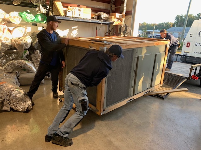 Three licensed technicians loading a 6 ton outdoor unit onto a trailer attached to a licensed contractor's truck.